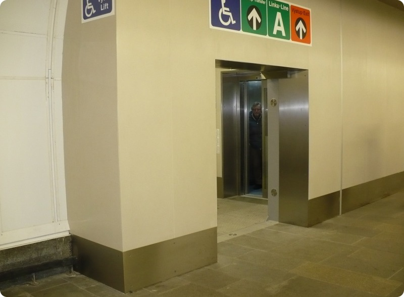 Výklenek pro výtah v široké přestupní chodbě dole k nástupišti trasy B